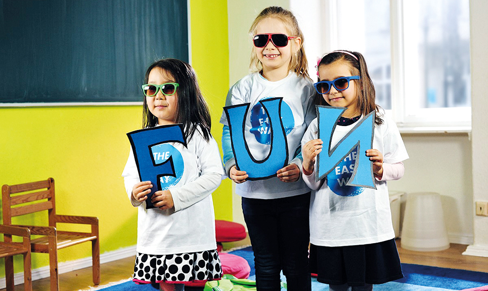 Kinder in einem Klassenzimmer mit großen Buchstaben die das Wort "Fun" bilden