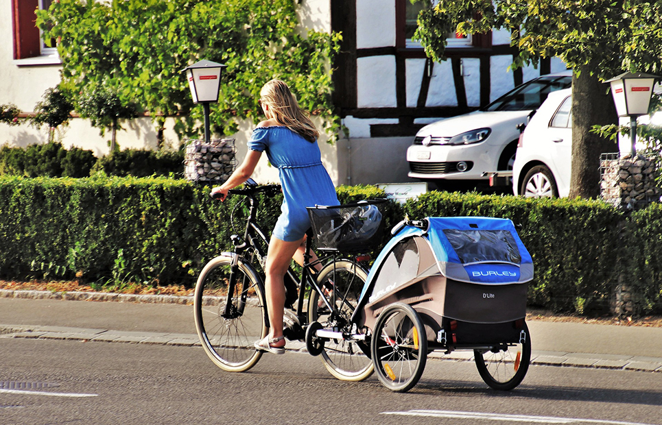 Frau fährt Fahrrad mit Kinderanhänger