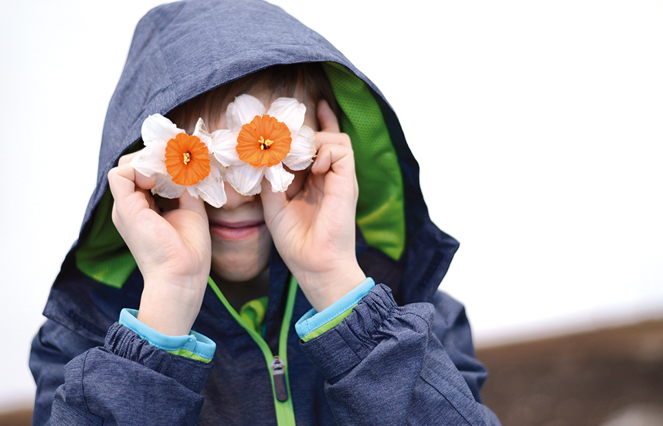 Junge hält sich zwei Narzissen-Blüten vor die Augen
