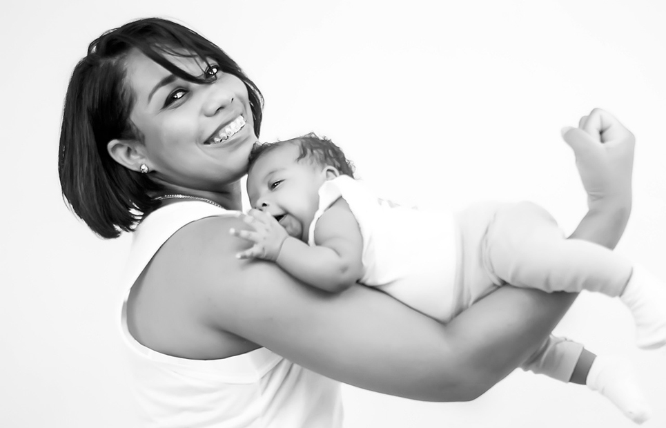 Mama in Fitnesspose mit einem liegenden Baby auf dem Oberarm