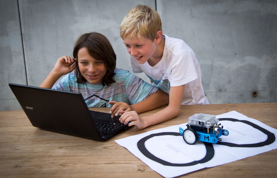 Zwei Jungen arbeiten zusammen an einem Laptop und programmieren eine Steuerung für einen Lego-Roboter