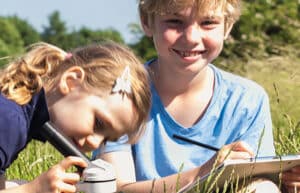 Ein Mädchen und ein Junge sitzen auf einer Wiese und experimentieren mit einem Mikroskop