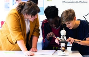 Man sieht zwei Schüler mit der Lehrerin am Mikroskop